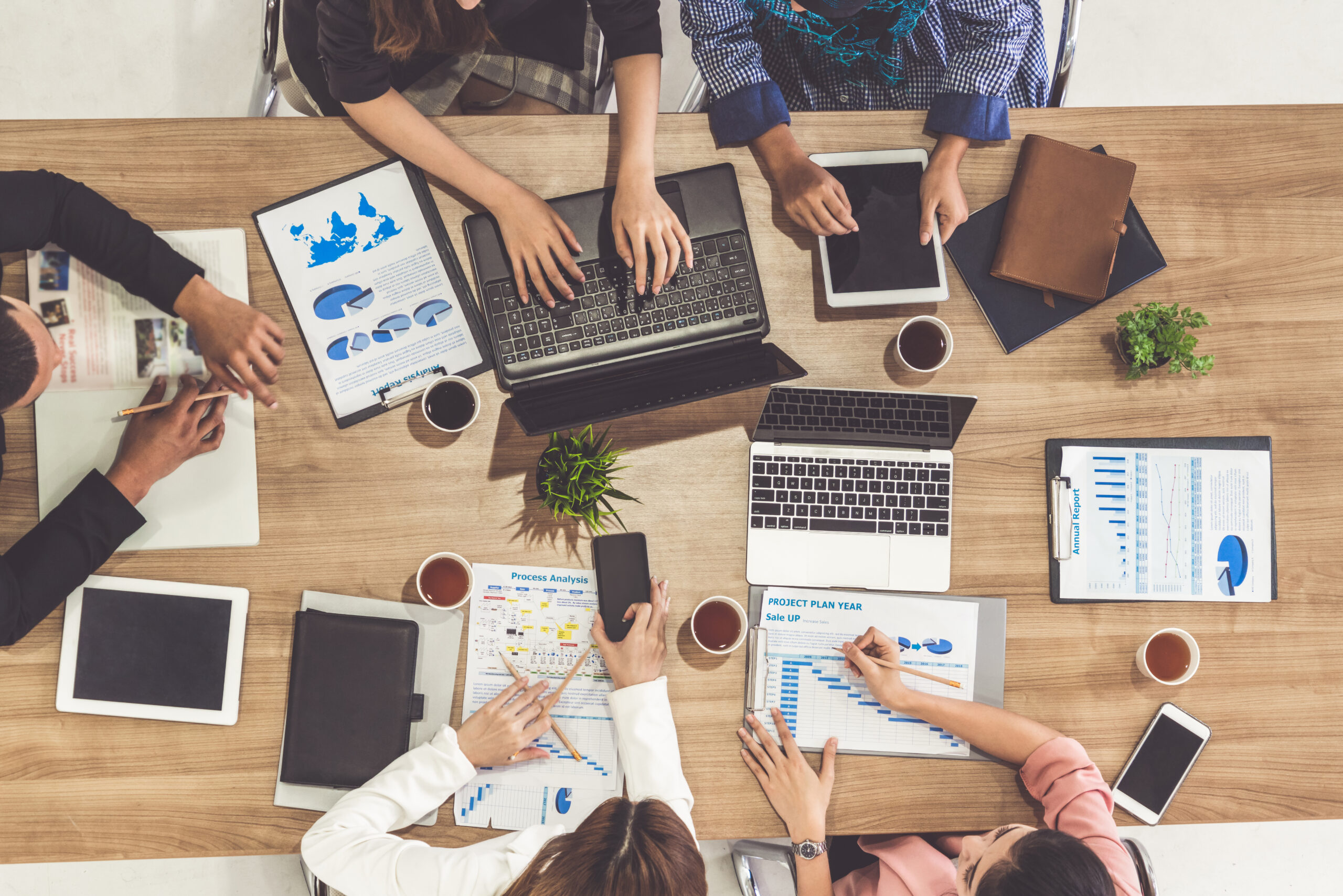 Top view of businessman executive in group meeting with other businessmen and businesswomen in modern office with laptop computer, coffee and document on table. People corporate business team concept.